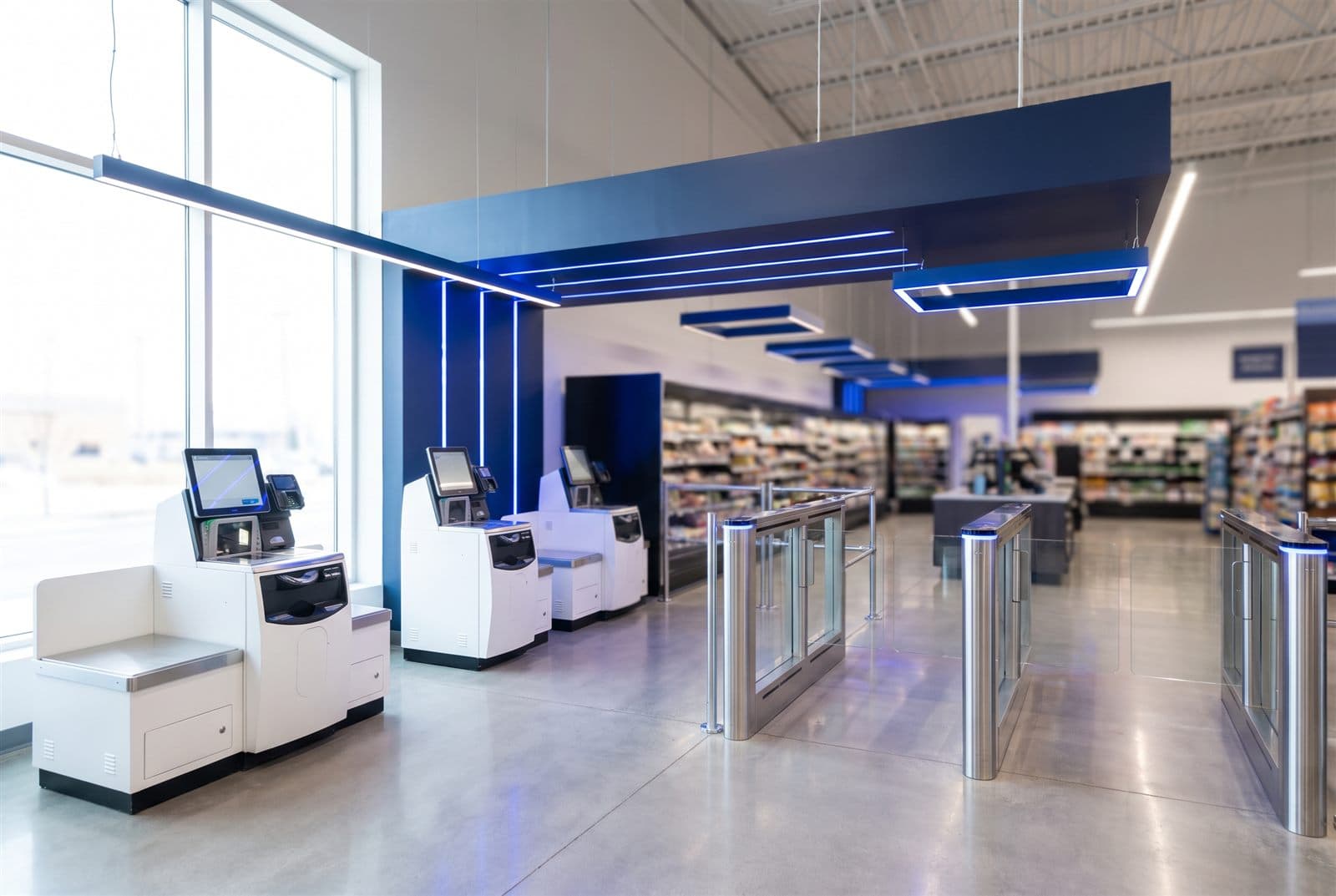 Moderne zelfscan-zone in een supermarkt met veel open ruimte rond de kiosken en poortjes — er kan makkelijk langs de zelfscankassa gelopen worden